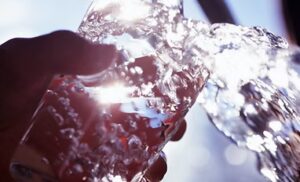Water splashing into a clear glass held up against a bright light, highlighting bubbles and reflections.